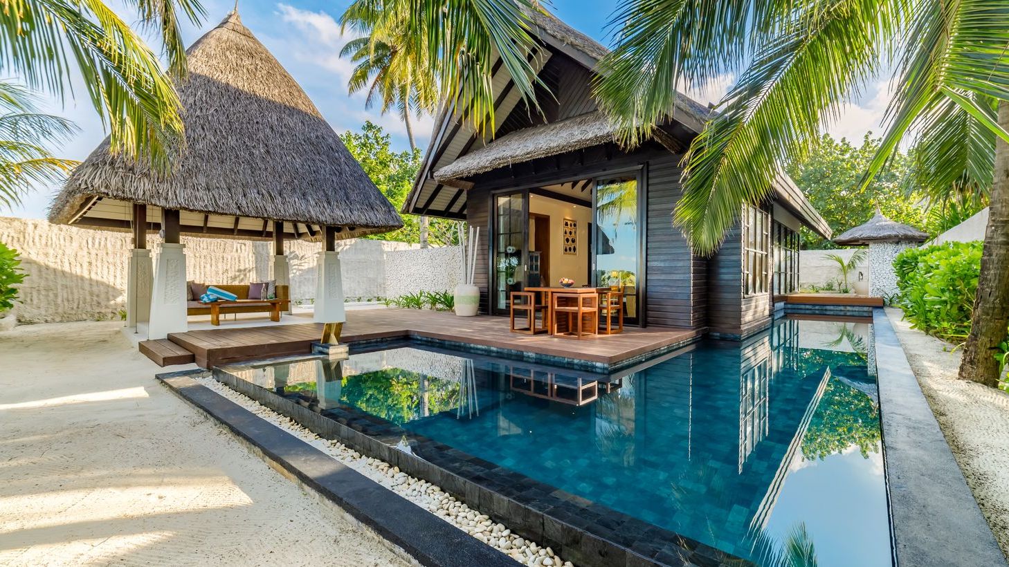Serene resort with a sparkling pool, thatched-roof villas, and lush greenery in Maldives.
