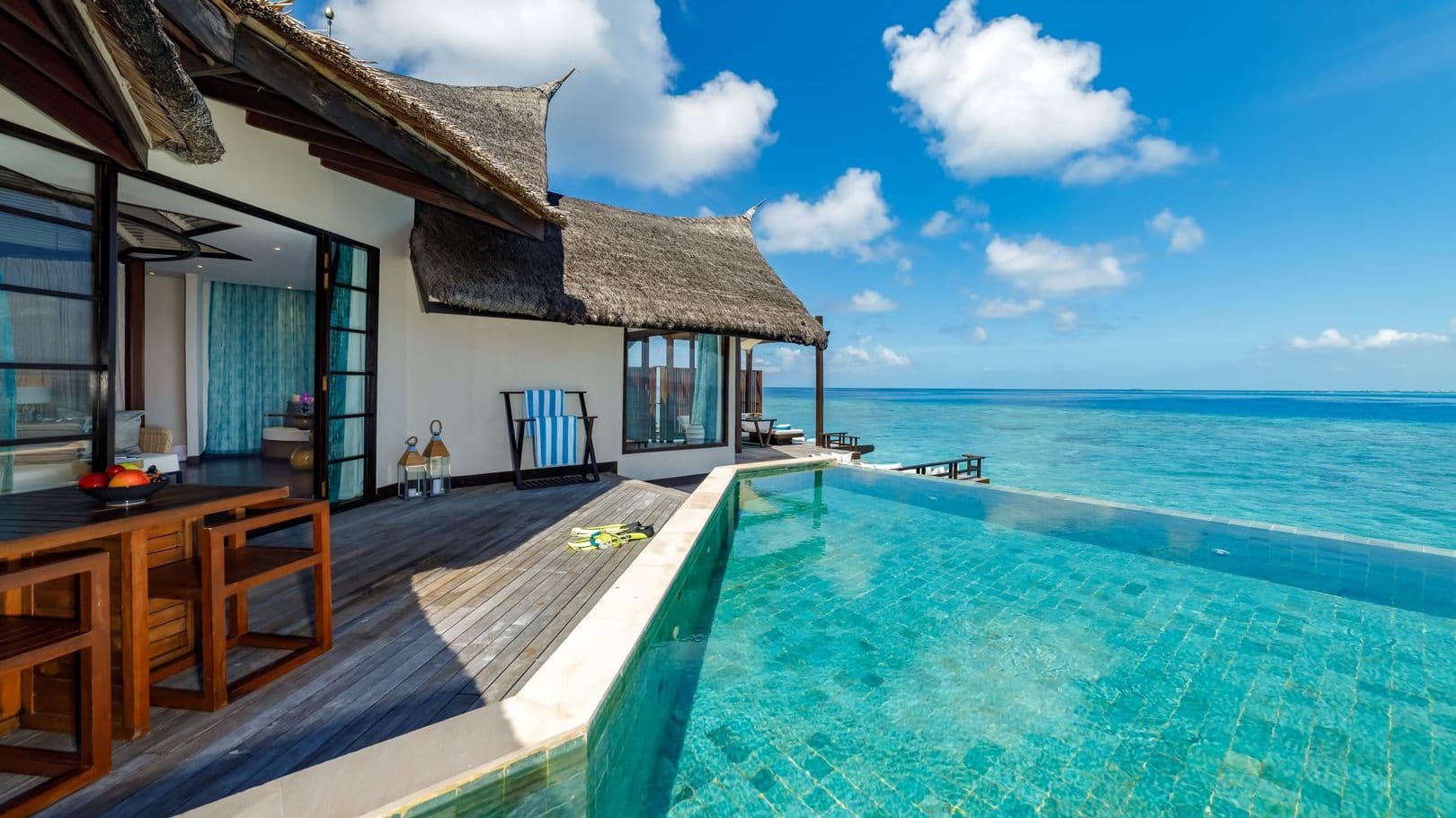 Luxury villas in Maldives with Ocean Pool Suite, tranquil pool and thatched huts under blue sky.