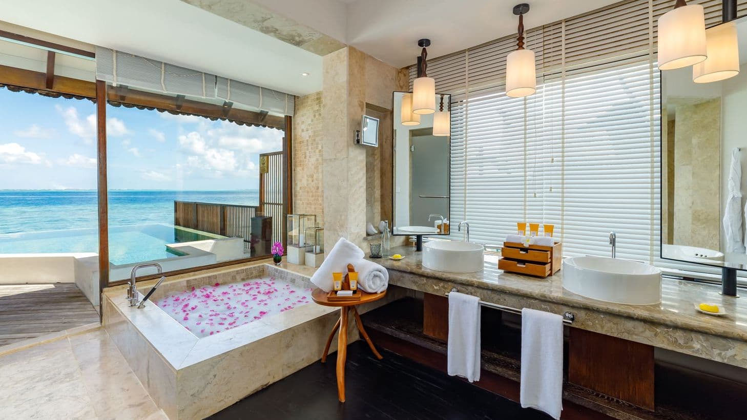 Luxury villas in Maldives with Ocean Pool Suite, tranquil pool and thatched huts under blue sky.