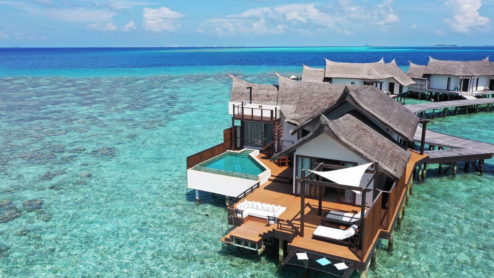Luxury villas in Maldives with Ocean Pool Suite, tranquil pool and thatched huts under blue sky.