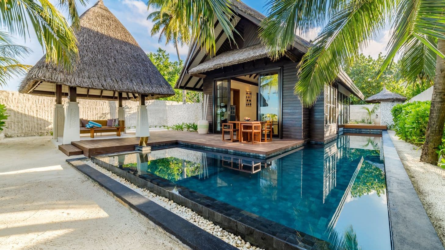 Serene resort with a sparkling pool, thatched-roof villas, and lush greenery in Maldives.