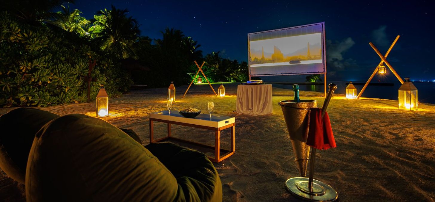 Movie under the Sky in Maldives with a bright screen on a peaceful beach at night.